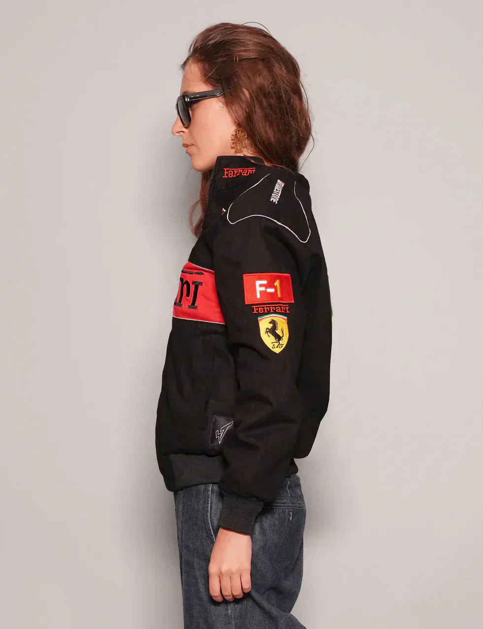 Person wearing a black jacket with Formula 1 logos on a plain background