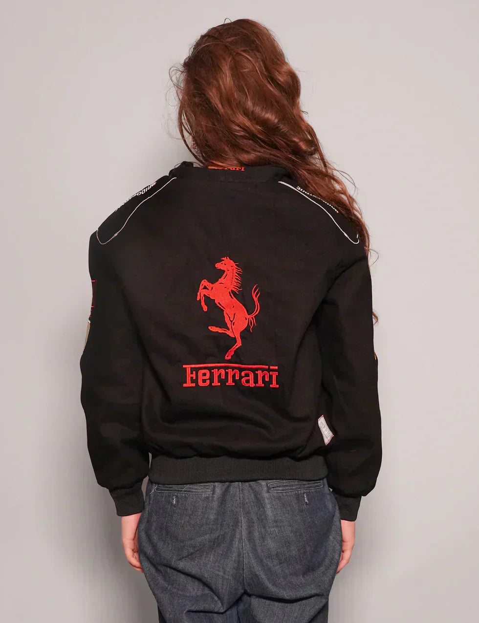 Person wearing a black Ferrari jacket with red logo on the back against a plain background