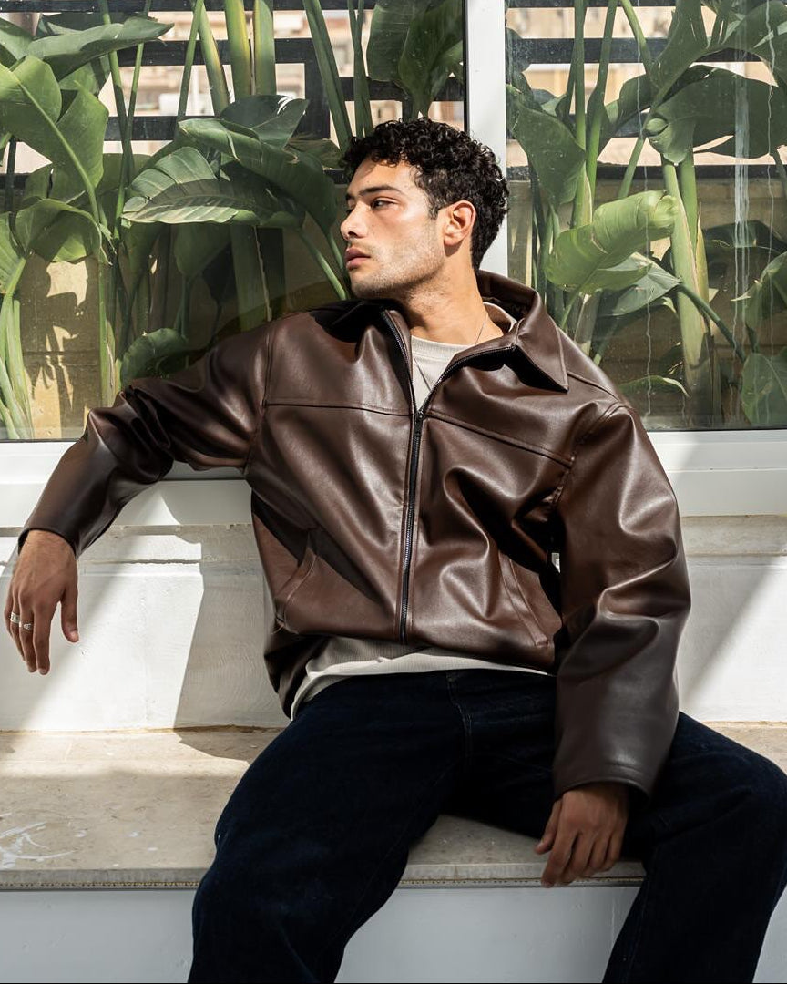 A man wearing a brown leather jacket and dark pants 