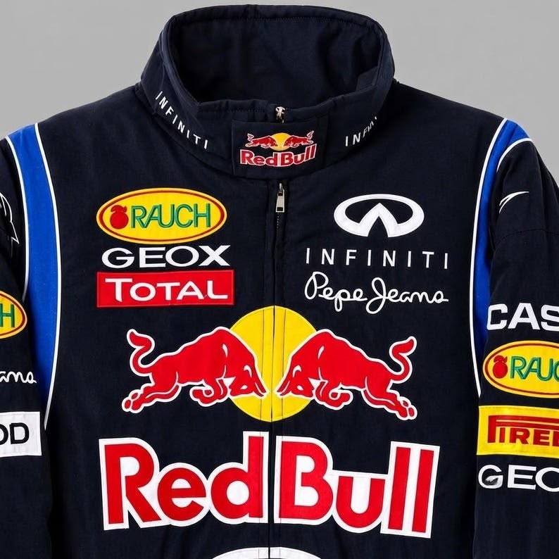 A navy blue Red Bull Racing team jacket featuring multiple sponsor logos including Red Bull, Infiniti, GeoX, Rauch, and Pirelli, with the iconic red bull logo on the front.