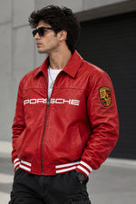 A man wearing a red leather Porsche bomber jacket with white 'PORSCHE' lettering on the chest and a Porsche crest patch on the sleeve, styled with black pants and sunglasses.